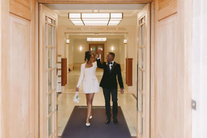 A couple walking arm in arm through the doorway of Hackney Town Hall on their wedding day